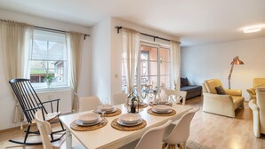 Un comedor con una mesa preparada para cuatro personas, una mecedora y un sofá en una habitación luminosa con ventanales grandes.