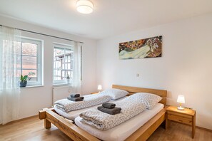Une chambre avec deux lits, une fenêtre avec des rideaux, un radiateur, une table de chevet avec une lampe et un tableau au mur.