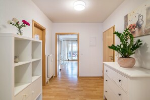 Un couloir avec un plancher en bois, des murs blancs, un radiateur, une plante en pot et un tableau.
