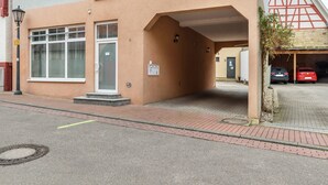 En bygning med et overdækket indgangsparti, en synlig dør og et lille udendørs område med en belagt sti.