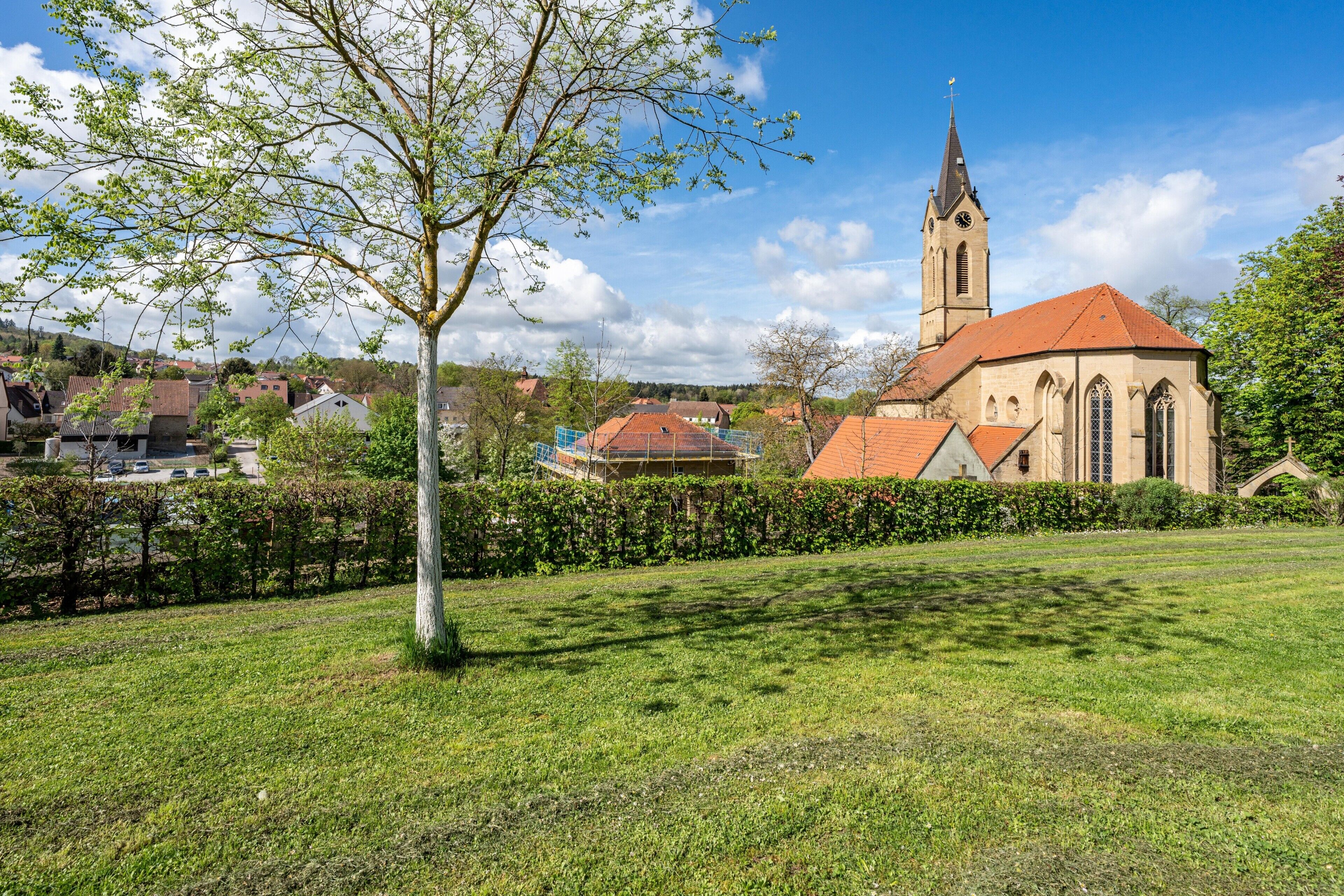 A church with a tall steeple, surrounded by a grassy area and a hedge.