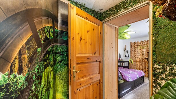 Habitació amb una porta de fusta, un llit amb estovatge morat i una paret coberta de verdura.