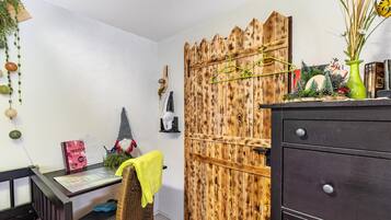 Ein Zimmer mit Holztür, Schreibtisch mit Stuhl, kleines Regal und Kommode.