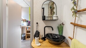 Un bany amb un tocador de fusta, un lavabo negre, un mirall i una barra de tovalloles.