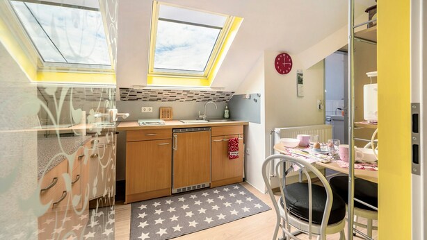 A compact kitchen with skylights, a dining area with a chair, and a visible radiator. - Picco 1: Modern Comfort Apartment with Balcony near Calmont Summit (Beuren)