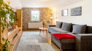 A living room with a stone wall, a grey sofa, a wooden cabinet, and a small table with a vase. - Picco 1: Modern Comfort Apartment with Balcony near Calmont Summit (Beuren)