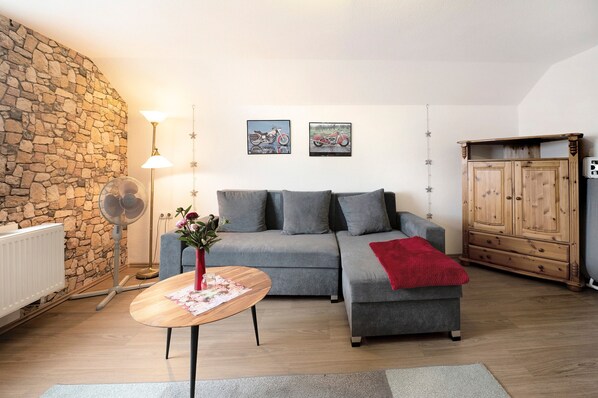 Un salon avec un mur en pierre, un canapé gris, un meuble en bois et un ventilateur.