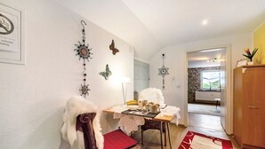 A dining area with a table set for two, a wicker chair with a red cushion, and a wall with decorative items. - Picco 1: Modern Comfort Apartment with Balcony near Calmont Summit (Beuren)