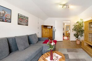 Un salon avec un canapé gris, un meuble en bois, une plante en pot et deux tableaux encadrés accrochés au mur.