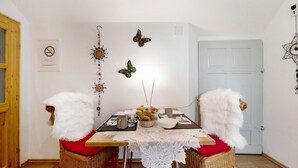 A dining area with a table set for two, surrounded by wicker chairs with white fur throws, a wall-mounted butterfly decoration, and a door with a star-shaped ornament. - Picco 1: Modern Comfort Apartment with Balcony near Calmont Summit (Beuren)