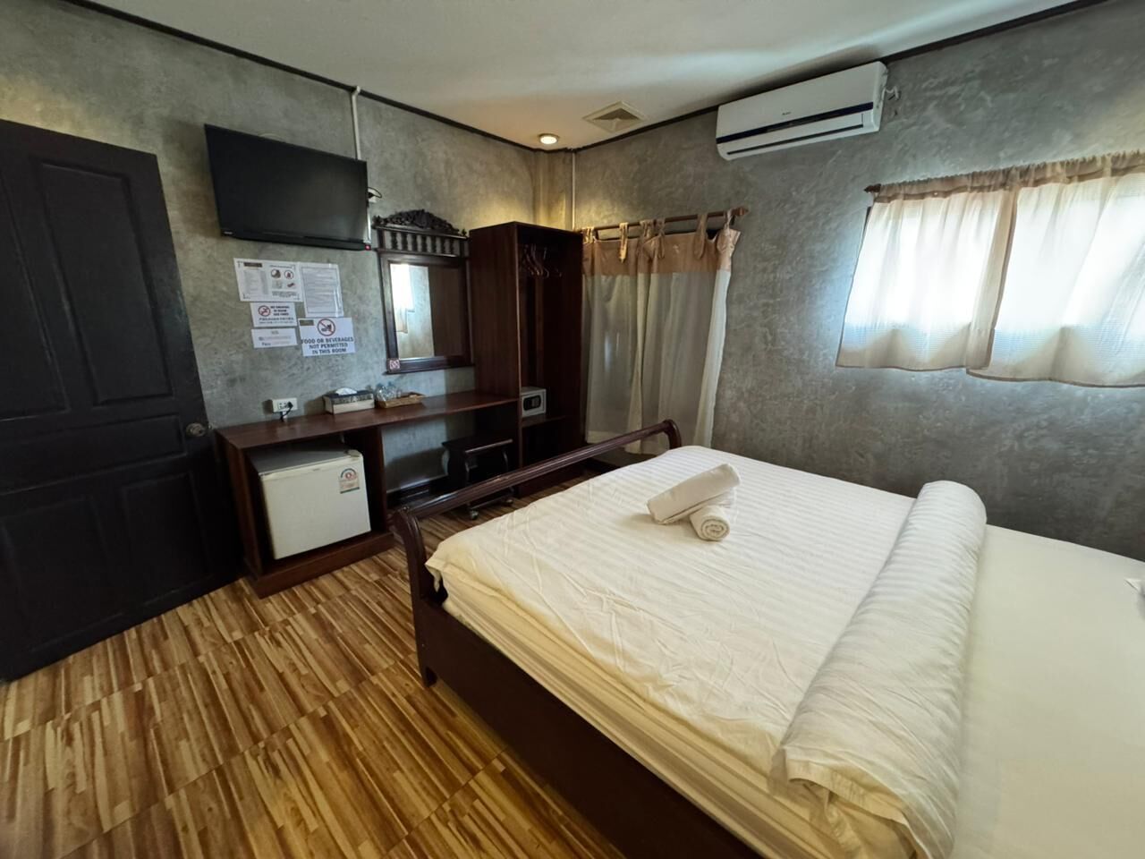 Habitación de hotel con cama, escritorio, espejo, armario y un refrigerador pequeño.