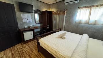 Habitación de hotel con cama, escritorio, espejo, armario y un refrigerador pequeño.