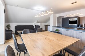 Une cuisine moderne dotée d’un four encastré, un coin repas avec une table en bois et des chaises noires, et un canapé noir dans l’espace salon.