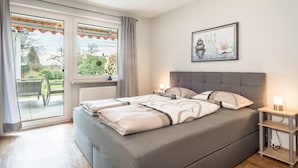 Ein Schlafzimmer mit Bett, Nachttisch, einem Bild an der Wand und Blick durch das Fenster.