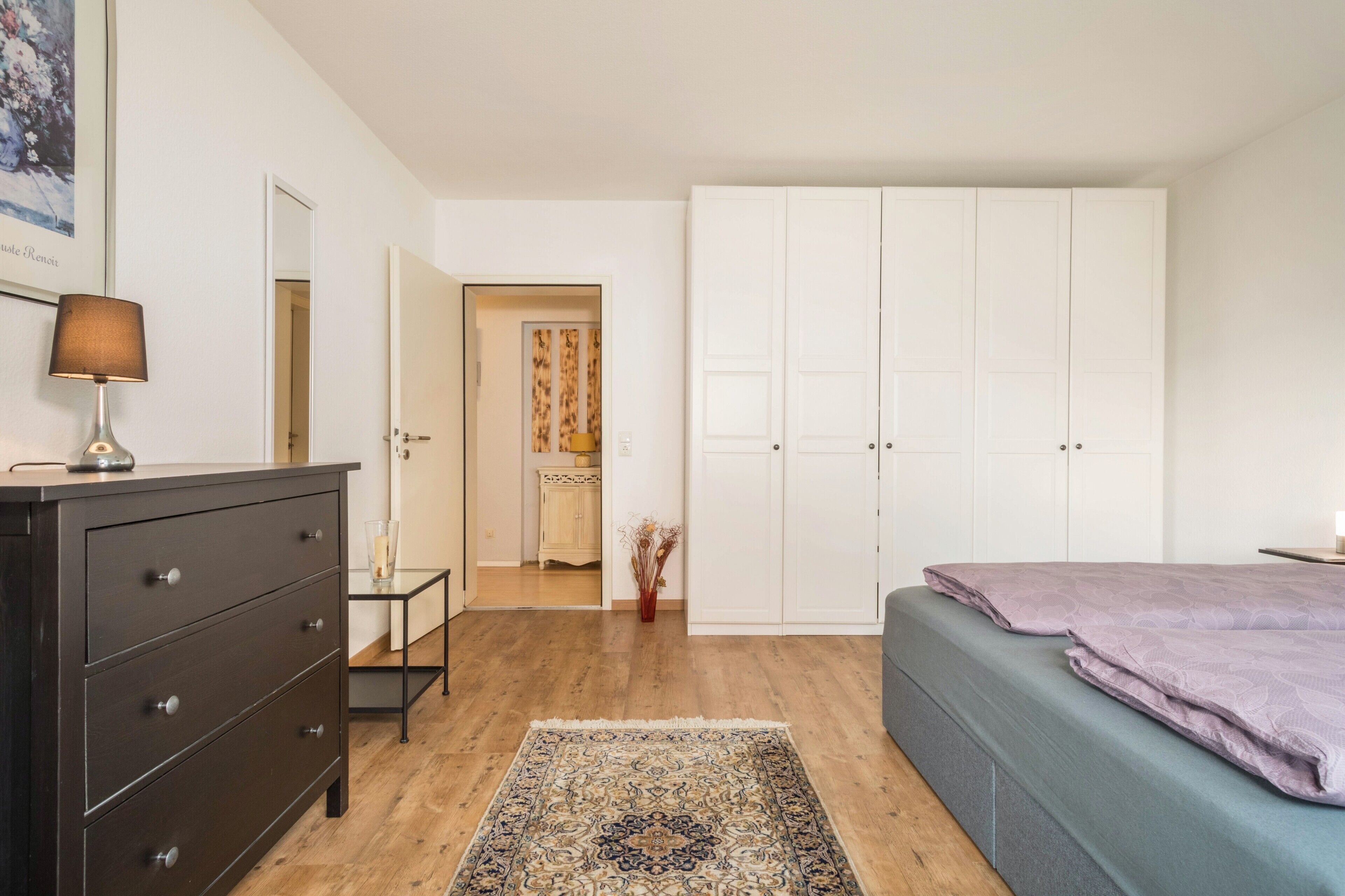 A bedroom with a bed, dresser, wardrobe, and a rug.