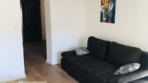 Uma sala de estar moderna com um sofá de couro preto, uma mesa de centro de madeira com comedouros de animais de estimação e um quadro abstrato colorido na parede.