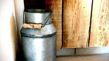 A metal container with a lid and handle, placed against a wooden wall and a tiled floor.