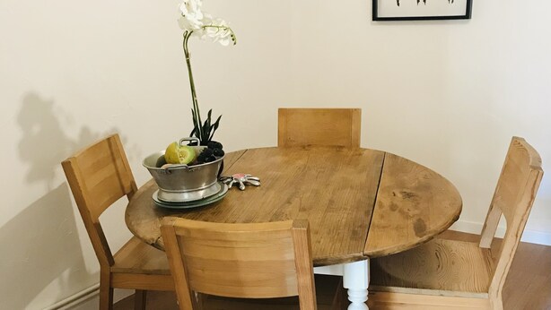 Uma mesa de jantar de madeira com quatro cadeiras, uma planta em vaso e um quadro na parede.