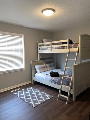 A bunk bed room with a ladder, a window with blinds, and a patterned rug on a wooden floor. - Nice CozyHome, Winston-Salem (Winston-Salem)