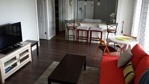 Ein Wohnzimmer mit Fernseher, einer Couch, einem Couchtisch und einem Essbereich mit Küche im Hintergrund.