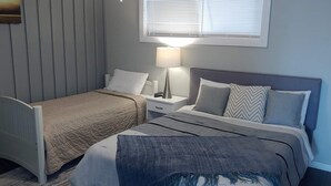Ein Schlafzimmer mit zwei Betten, einem Nachttisch mit Lampe und einem Fenster mit Jalousien.