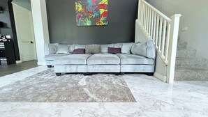 A living room with a grey sectional sofa, a patterned rug, marble flooring, a staircase, and a colorful abstract painting on the wall. - Luxury Gated Retreat – Resort Amenities, Pool, Spa, Gym (Mesa)