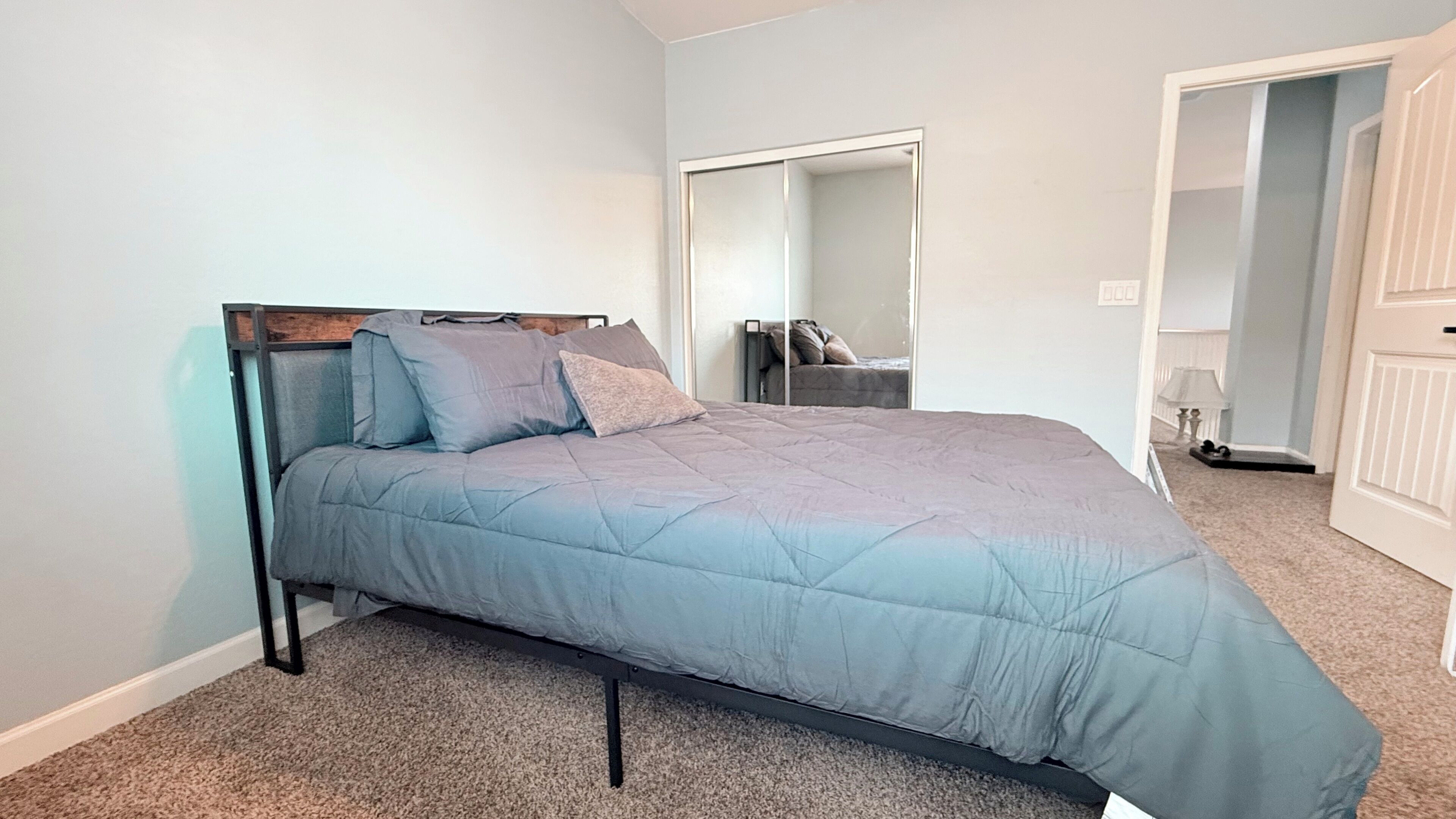 Un dormitorio con cama, espejo y puerta.