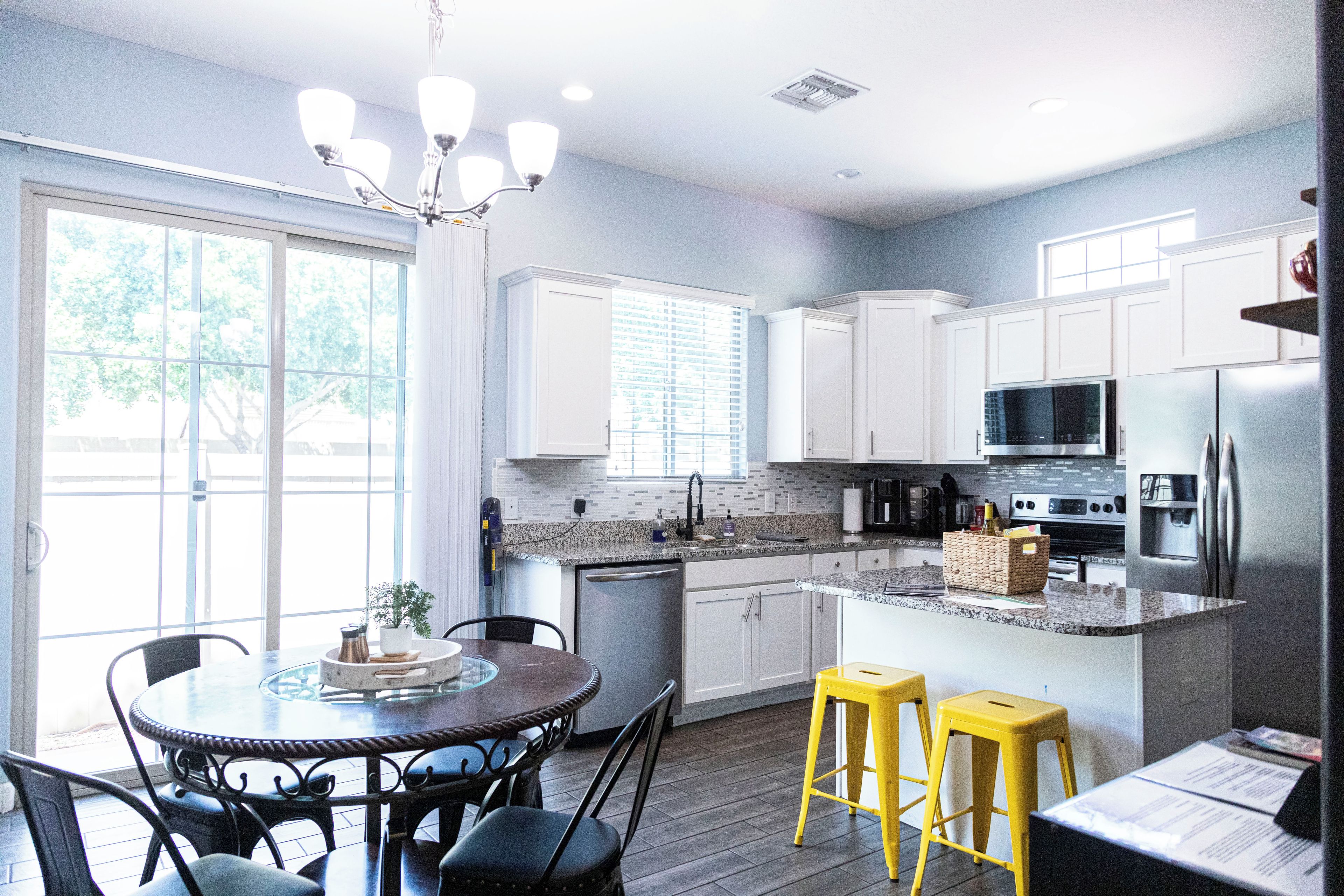 A modern kitchen with white cabinets, a granite countertop, stainless steel appliances, and a dining area with a round table and chairs.