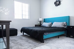 Un dormitorio con cama, mesita de noche, lámpara y ventana con persianas.