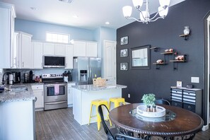 Una cocina moderna con armarios blancos, electrodomésticos de acero inoxidable, una isla central con taburetes y una mesa de comedor.