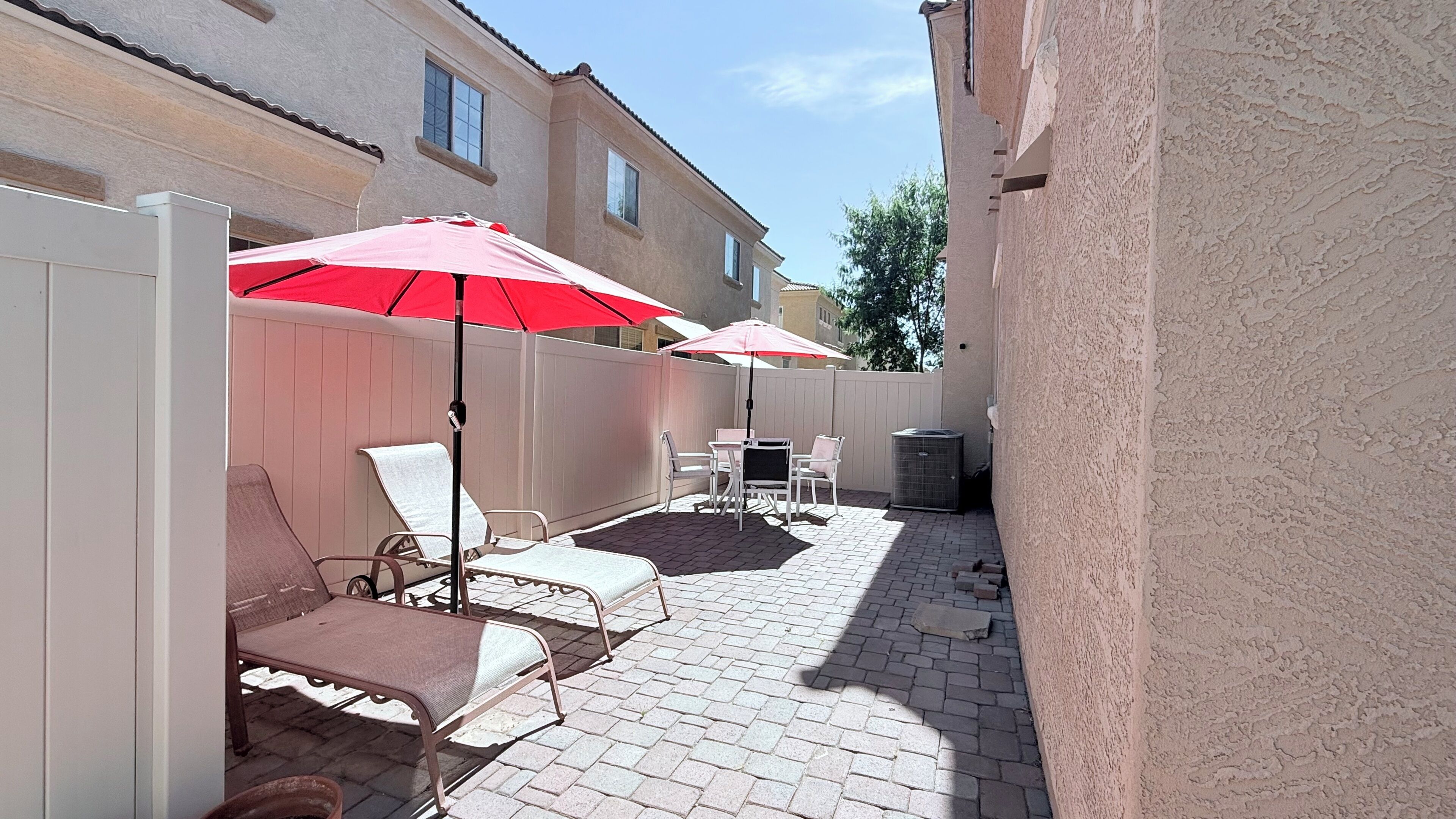 Un patio con mobiliario exterior, dos sombrillas rojas y piso de ladrillo.
