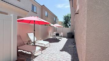 Un patio con mobiliario exterior, dos sombrillas rojas y piso de ladrillo.