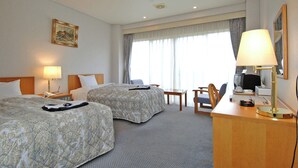 Hotellihuone, jossa on kaksi sänkyä, työpöytä, tuoli, lamppu ja taulu seinällä.