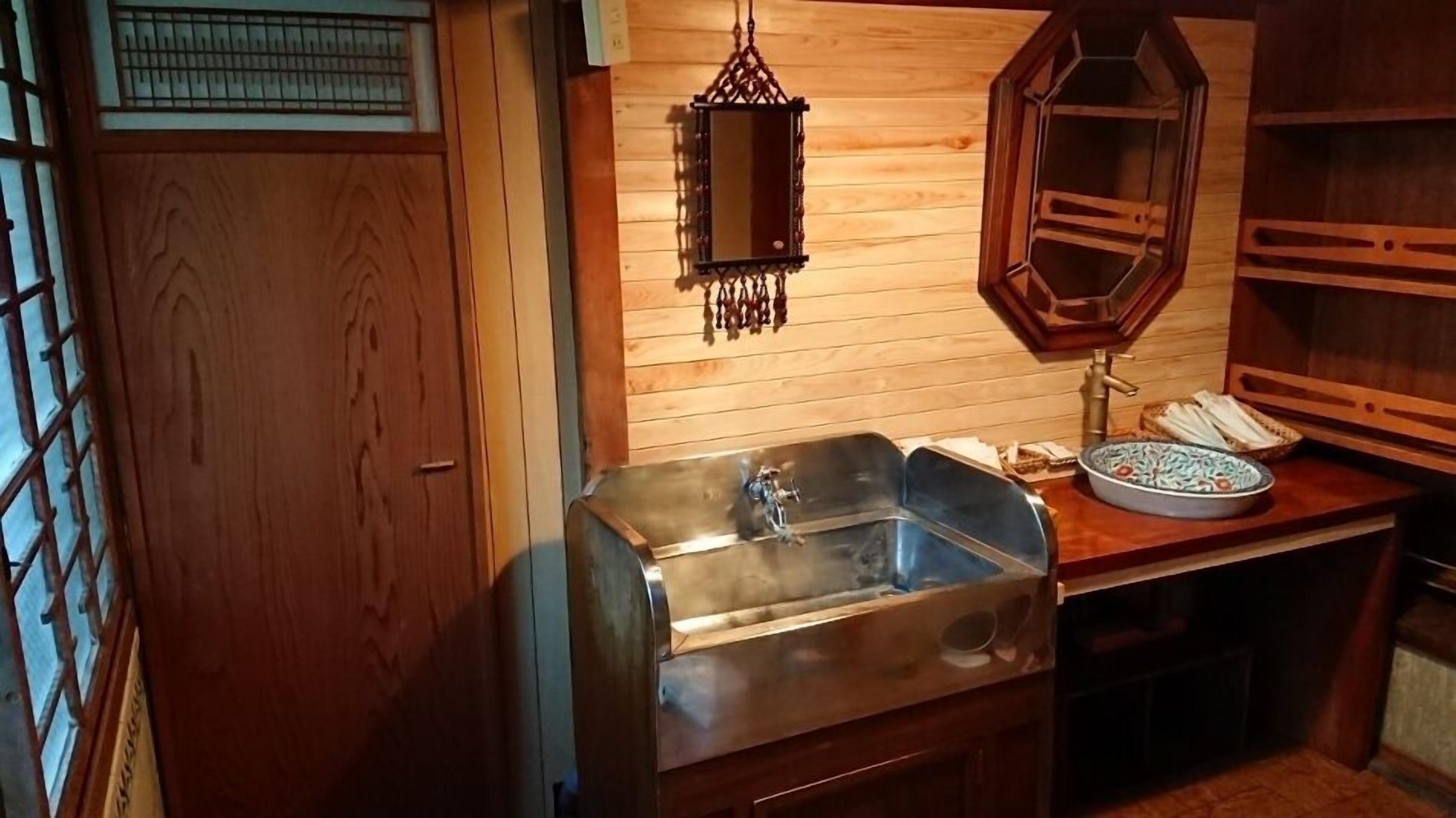 A wooden interior with a sink, a hanging mirror, and a small table with a bowl and a telephone.
