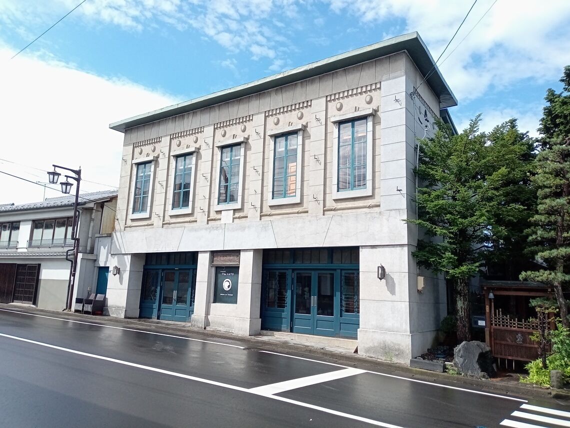 A two-story building with a flat roof, large windows, and a blue door.