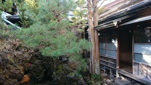 En traditionell japansk byggnad med en träfasad, en stenträdgård och ett tallträd.