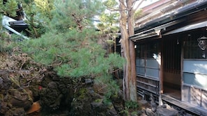 A traditional Japanese building with a wooden exterior, a rock garden, and a pine tree.