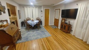 A dining area with a round table and chairs, a wooden cabinet, a television, and a patterned rug. - Self Check-In & Free Wi-Fi in this Fresh Remodel! (Idaho Falls)