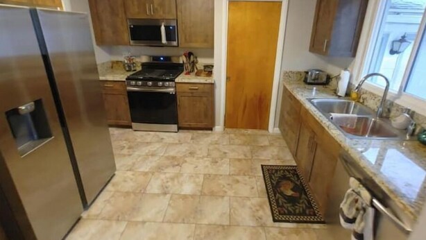 A kitchen with wooden cabinets, a stainless steel refrigerator, a microwave, a stove, and a sink. - Self Check-In & Free Wi-Fi in this Fresh Remodel! (Idaho Falls)