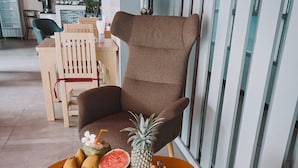 A modern living room with a brown armchair, a small round table with a fruit tray, and a lamp on a stand. - Natalie House Kata Beach (Karon)