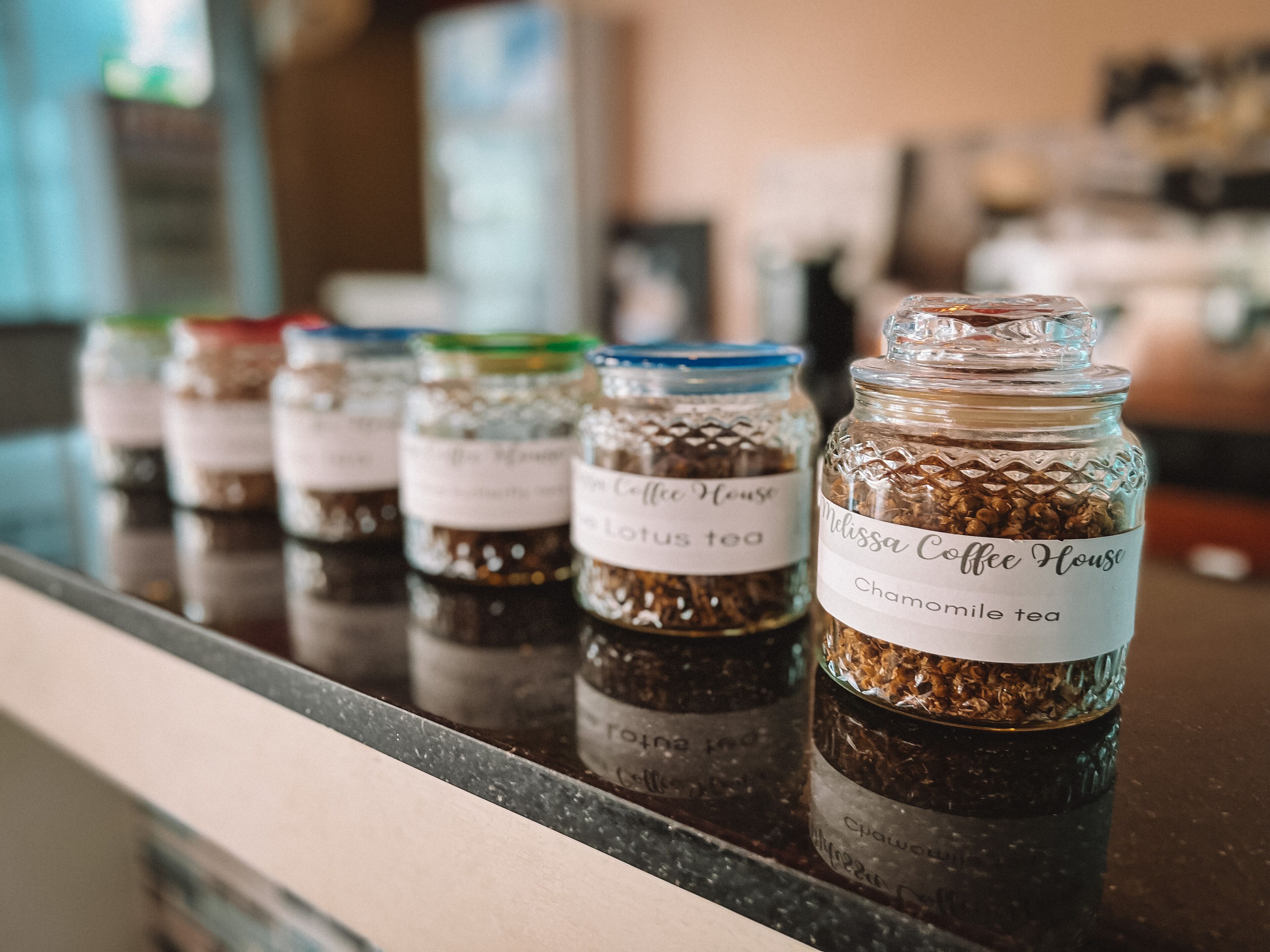 A row of glass jars labeled with different types of tea on a reflective countertop.