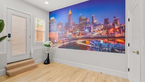 A hallway with a cityscape mural, wooden flooring, a staircase, and a vase with flowers.