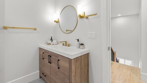 A bathroom with a white vanity, wooden cabinets, a gold-framed mirror, and two wall-mounted light fixtures.