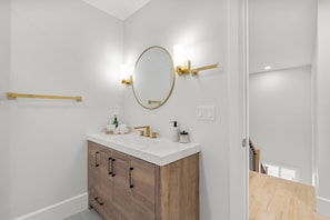 A bathroom with a white vanity, wooden cabinets, a gold-framed mirror, and two wall-mounted light fixtures.