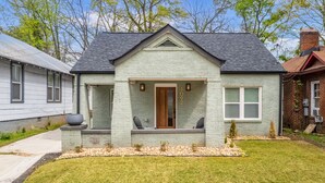 A single-story house with a gabled roof, a front porch with two chairs, and a small garden area.