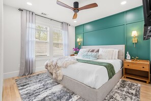 A bedroom with a bed, a ceiling fan, a nightstand, and a window with curtains.