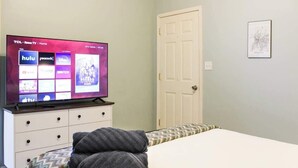 Un dormitorio con una televisión mostrando servicios de streaming, una puerta blanca y un cuadro en la pared.
