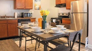 Una cocina moderna con armarios de madera, un refrigerador de acero inoxidable y una mesa de comedor preparada para cuatro comensales.
