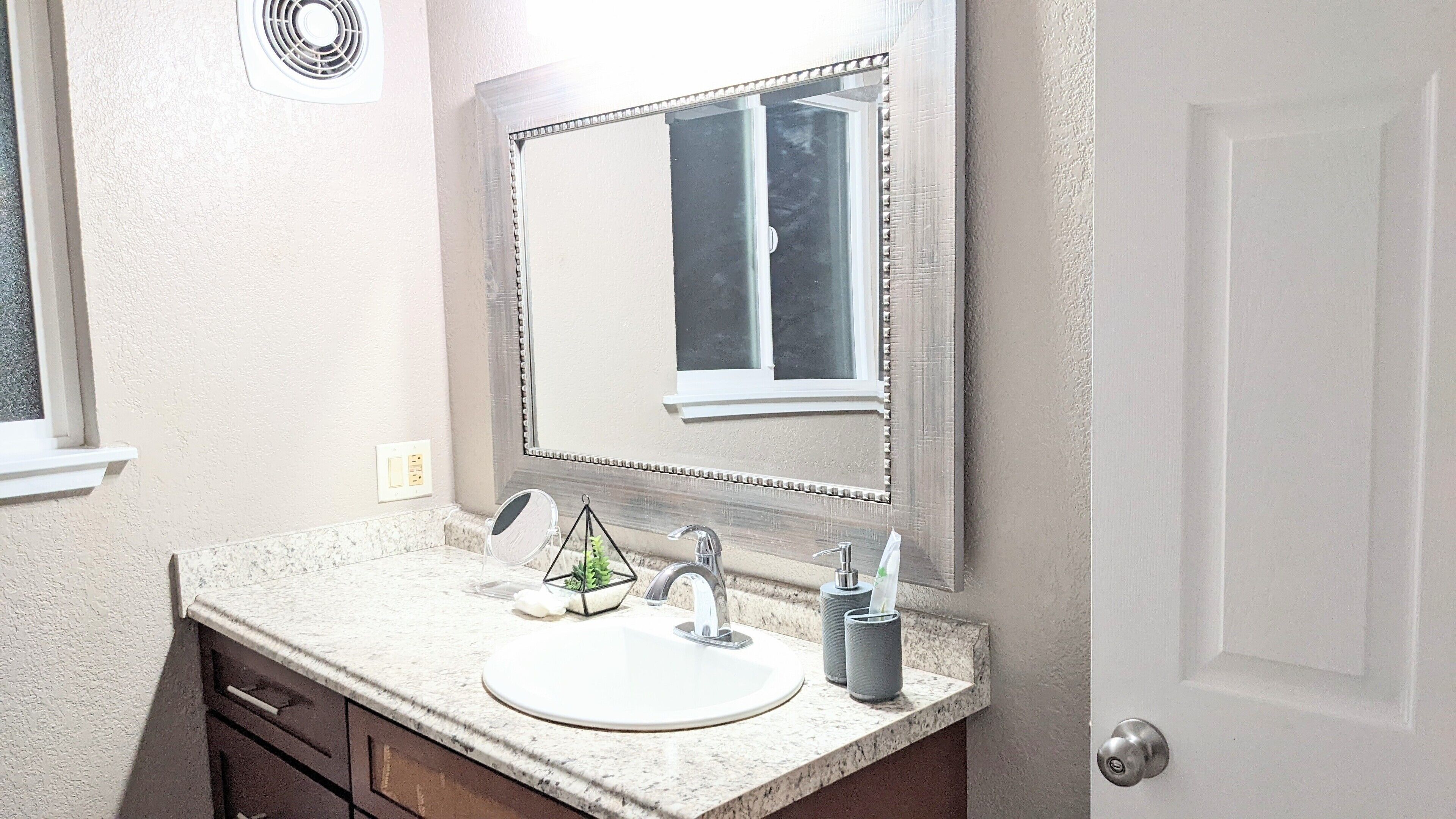 A bathroom with a white sink, two faucets, a mirror, and a window.