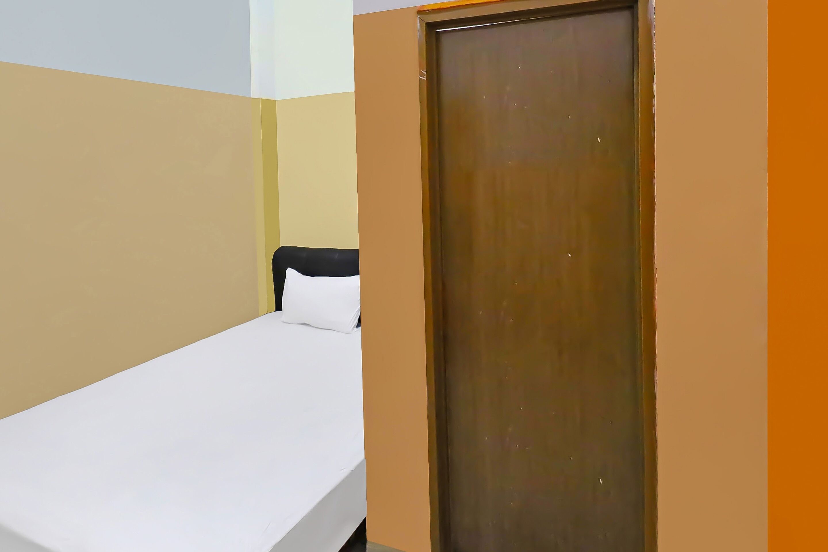A small, single-bed room with a wooden door and a white mattress.